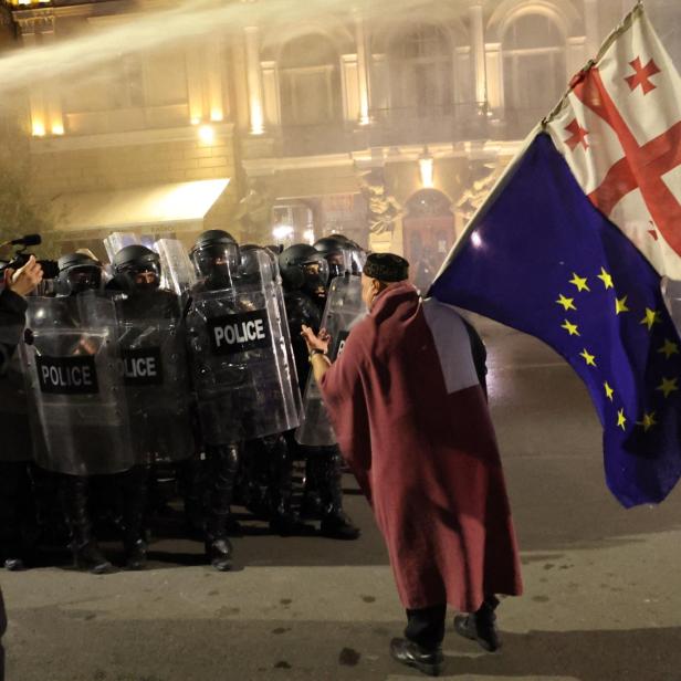 Ein Mann steht mit EU und Georgien-Flagge vor Anti-Riot-Polizisten.