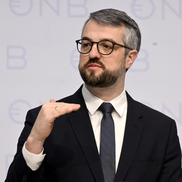 Mann mit Anzug, Bart und Brille vor einer weißen Wand mit OeNB-Logo.