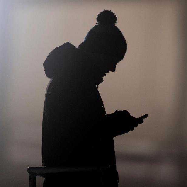 Ein Mann schaut auf ein Smartphone und zeichnet sich als Silhouette ab. 