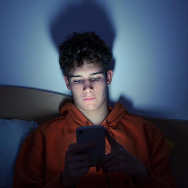 Teenager mit Smartphone liegend im Bett in der Nacht
