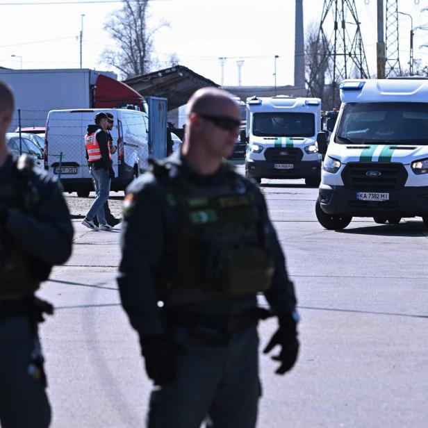 Zwei Beamte der ungarischen Spezialeinheit TEK, dahinter die beiden beschlagnahmten Geldtransporter.