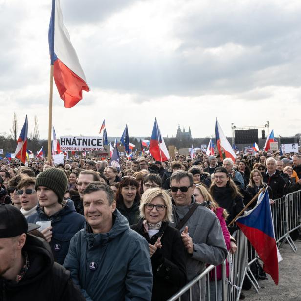 Große Demonstration unter grauem Himmel, einzelne rot-weiß-blaue Flaggen ragen über die Menschenköpfe hinaus 