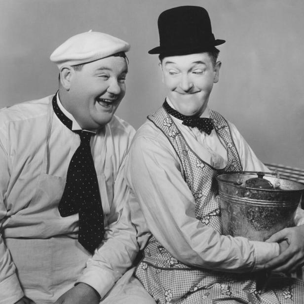 Der Hollywood-Comedian Oliver Hardy lacht seinen ebenfalls fröhlich aussehenden Kollegen Stan Laurel treuherzig an