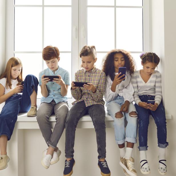 Fünf Kinder sitzen nebeneinander auf einer Fensterbank und schauen auf ihre Smartphones