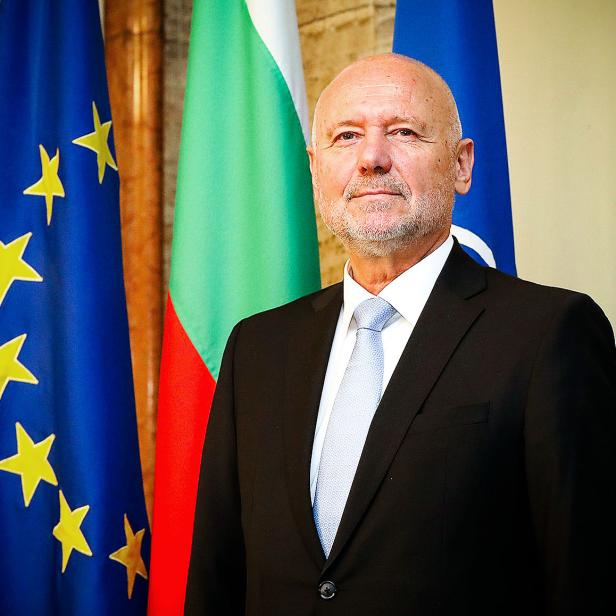 Ein Mann im Anzug steht vor den Flaggen der EU, Bulgariens und der NATO.