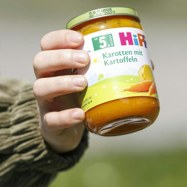 Eine Hand hält ein Glas Babynahrung mit der Aufschrift „Karotten mit Kartoffeln“ von HiPP.