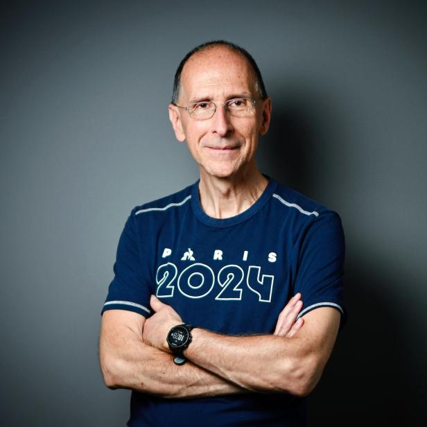 Peter Filzmaier steht in einem Sportleiberl vor grauem Hintergrund