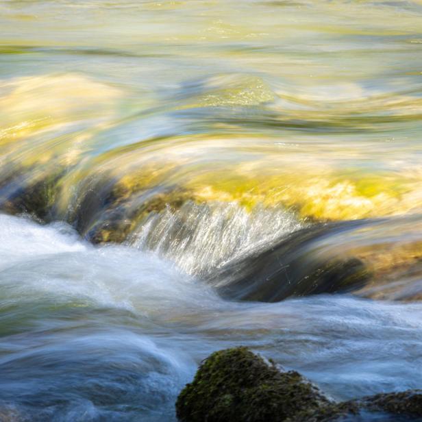 Fließendes Wasser mit kleinen Wellen und Felsen im Vordergrund