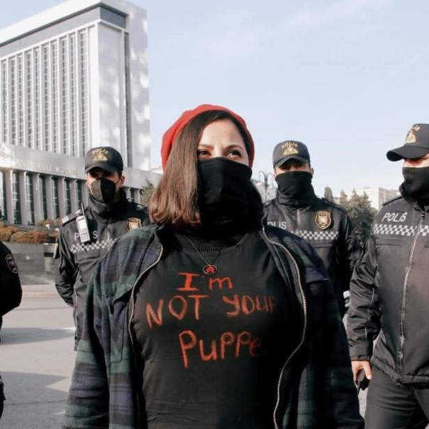 Ulviyya Guliyeva steht vor fünf Polizisten. Sie trägt ein Shirt mit der Aufschrift "I'm not your puppy".