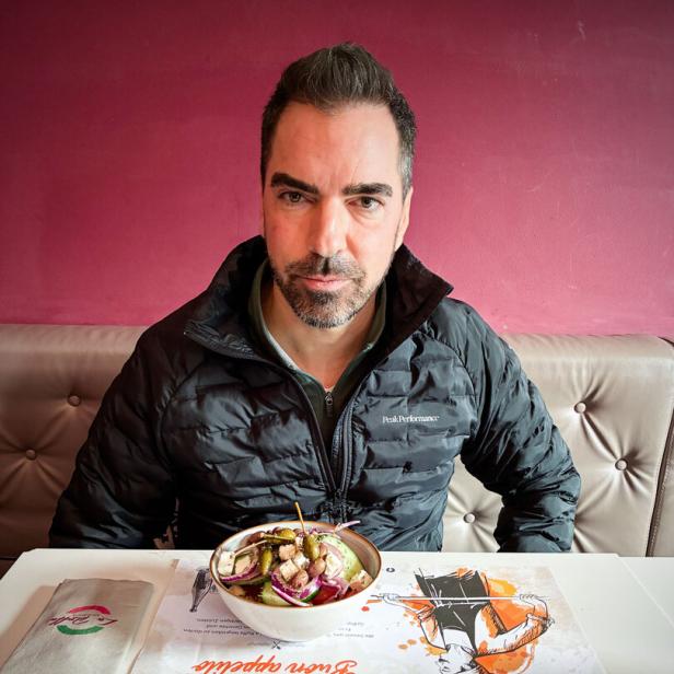 Unternehmer Karl Ochsner sitzt in einer Daunenjacke in einer Pizzeria, vor sich am Tisch ein Salat