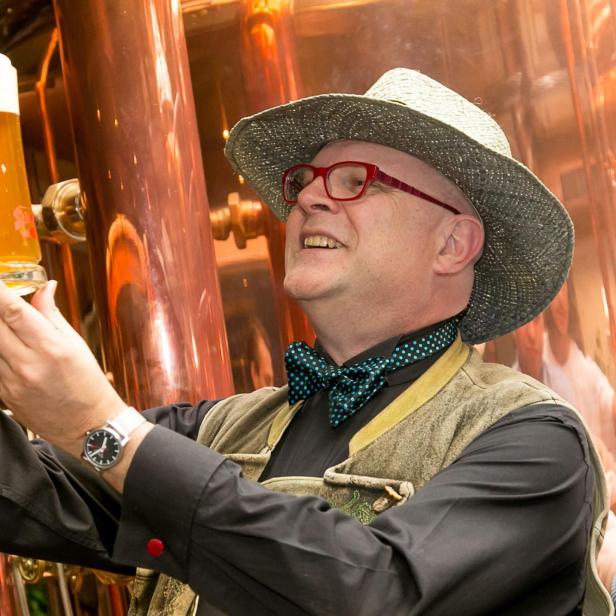 Bierkenner Conrad Seidl mit Hut begutachtet vor einem Braukessel ein frisch gezapftes Bier