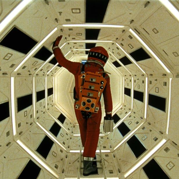 Mann in orangem Raumanzug durchquert einen hellen futuristischen Korridor