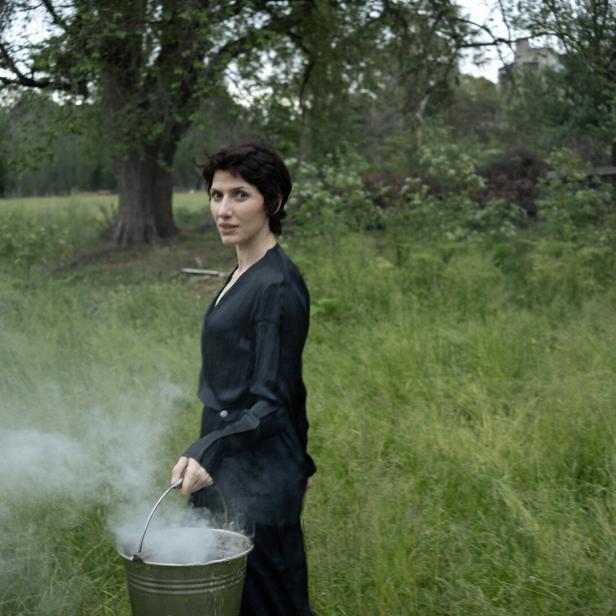 Die Musikerin Aldous Harding trägt einen Kübel, aus dem Dampf strömt, durch eine grüne Waldlandschaft.