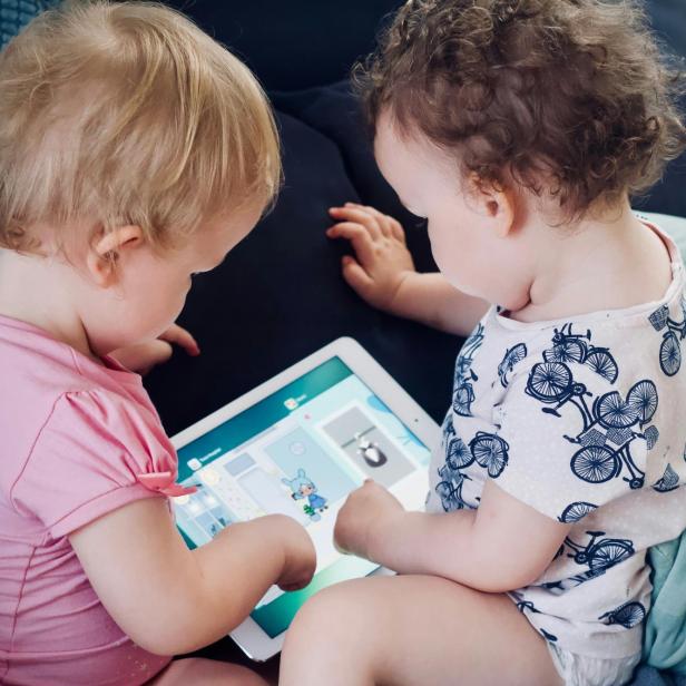 zwei Kleinkinder sitzen auf dem Sofa, während sie einen Tablet-Computer benutzen