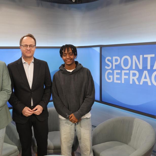 Drei Personen stehen vor einem Bildschirm mit der Aufschrift 'SPONTAN GEFRAGT' in einem Fernsehstudio