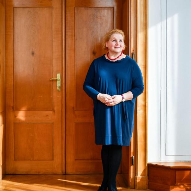 Eine Frau im blauen Kleid, es ist Sozialministerin Schumann, steht vor einer braunen Tür