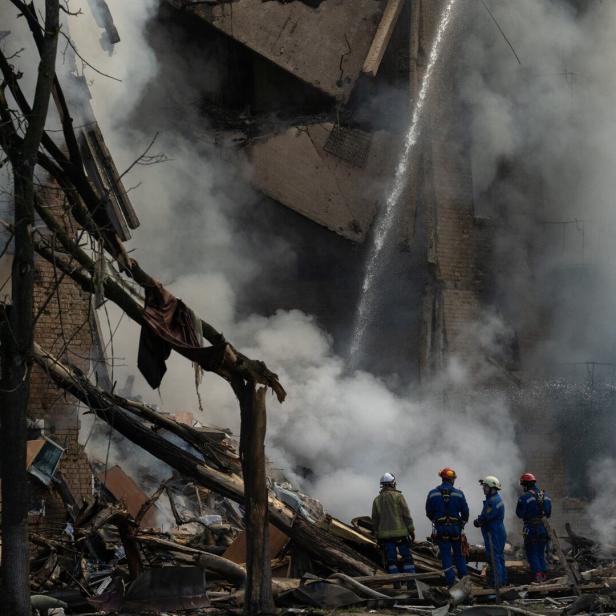 Feuerwehrmänner stehen vor einem zerstörten Haus, Rauch steigt auf