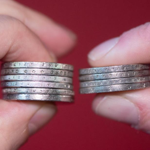 Zwei Hände halten Euro-Münzen zwischen den Fingern.