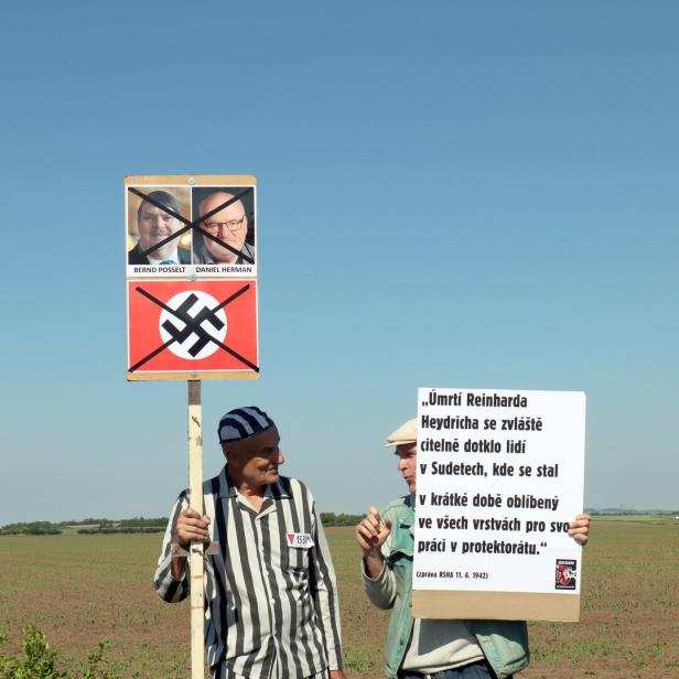 Ein Mann verkleidet als KZ-Häftling hält ein Plakat mit durchgestrichenem Hakenkreuz hoch.