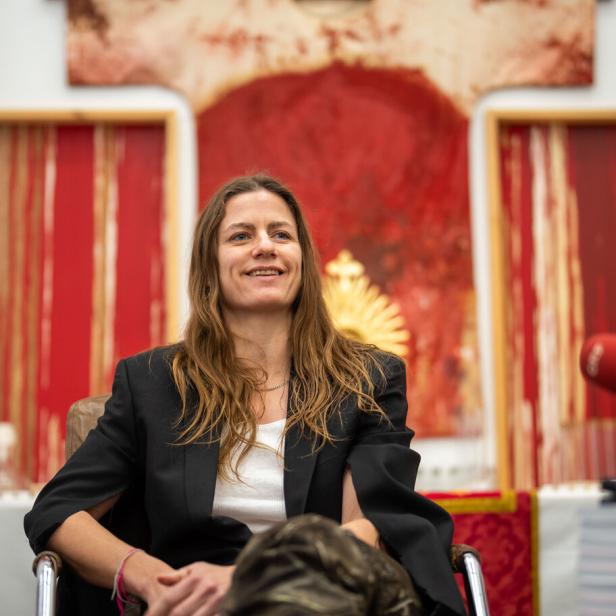 Die Künstlerin Florentina Holzinger lächelt, im Hintergrund Schüttbilder des Aktionisten Hermann Nitsch