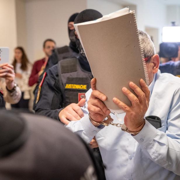 Khaled H. verdeckt sein Gesicht mit einer Mappe, er ist umringt von Polizeibeamten.