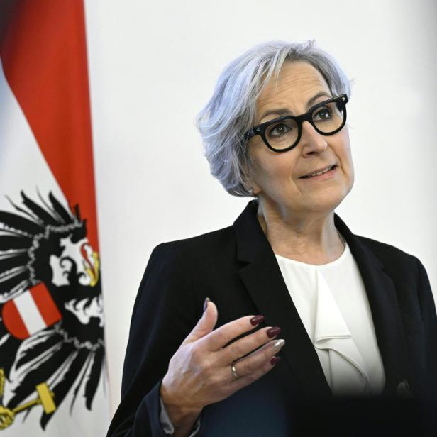 Die österreichische Justizministerin Anna Sporrer spricht vor einer österreichischen Flagge.
