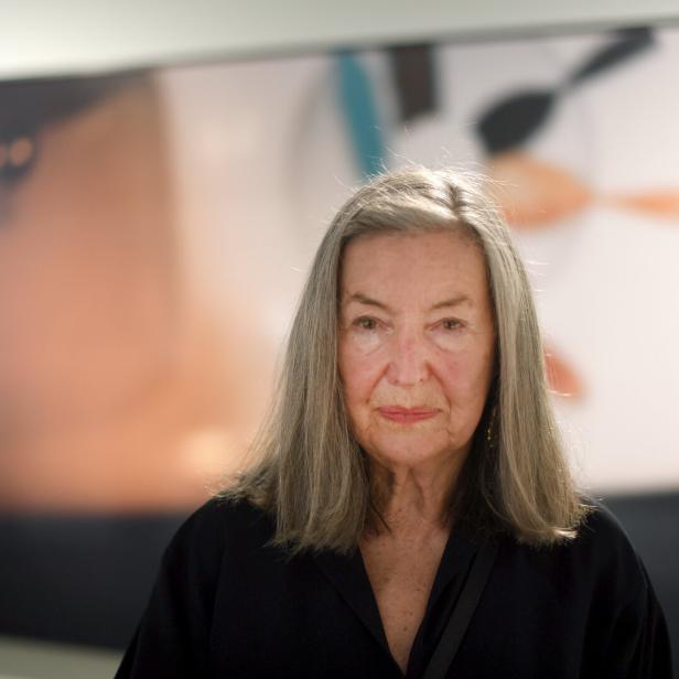 Die Fotografin Elfie Semotan blickt ernst in die Kamera, im Hintergrund unscharf ein buntes Kunstwerk