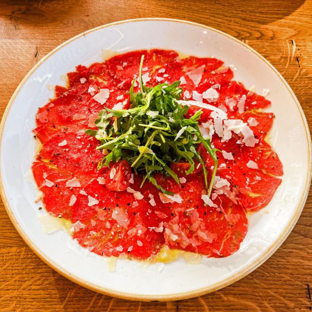 Das Bild zeigt ein Rinder-Carpaccio mit Parmesan, Olivenöl und Rucola
