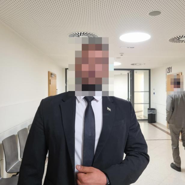 Zeuge Achmad in Anzug in einem Gang des Wiener Landesgericht, sein Gesicht ist verpixelt.