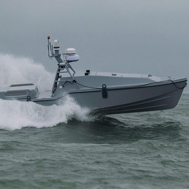 Eine "Corsair"-Drohne (ein graues Motorboot, mit auffälligem Radarsystem) fährt auf dem Wasser und hinterlässt eine große Welle hinter sich.