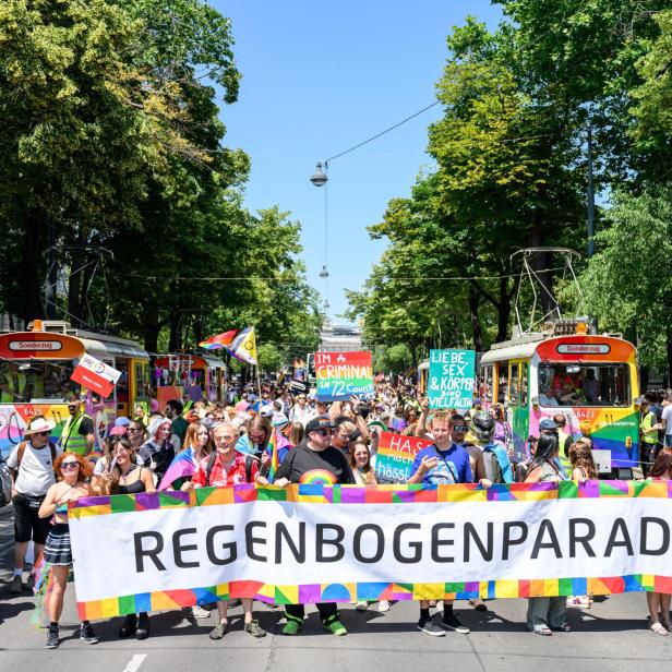 Viele Protestierende auf die Vienna ride Regenbogenparade halten einen großen banner. Im Hintergrund sind bunte Fahnen.