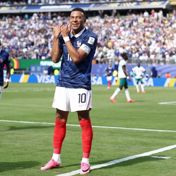 Kylian Mbappe steht auf dem Fußballplatz und jubelt über ein Tor, indem er eine Flötenbewegung macht