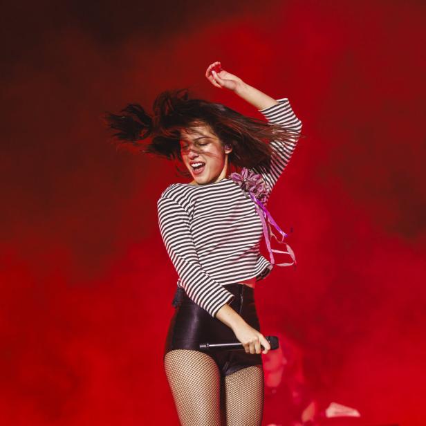Popstar Olivia Rodrigo springt auf der Bühne vor rot beleuchteten Trockeneisschwaden. 