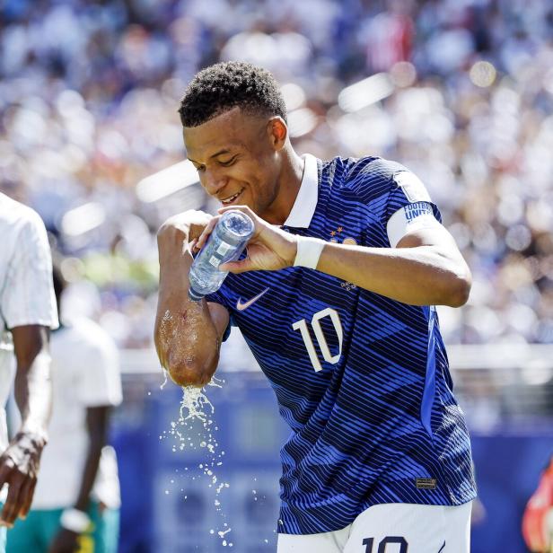 Kylian Mbappe schüttet sich während eines Fußballspiels Wasser aus einer Trinkflasche auf den Arm