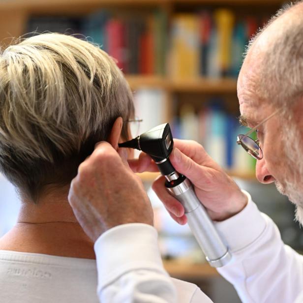 Ein Arzt untersucht mit einem Otoskop das Ohr einer Patientin in einer Praxis.
