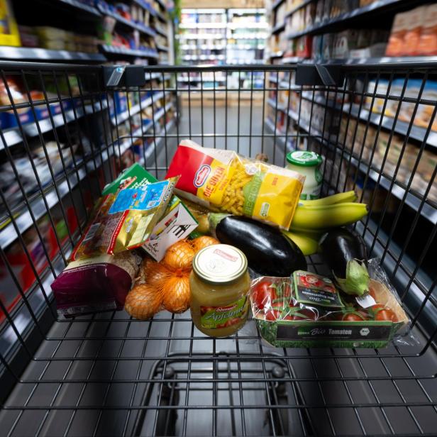Einkaufswagen mit Produkten wird durch Supermarkt geschoben.