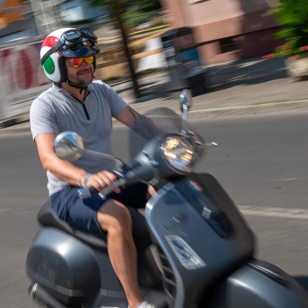 Ein Mann fährt auf einem Roller mit Helm durch eine Straße.