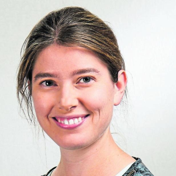 Porträt einer lächelnden Frau mit zusammengebundenem Haar vor hellem Hintergrund