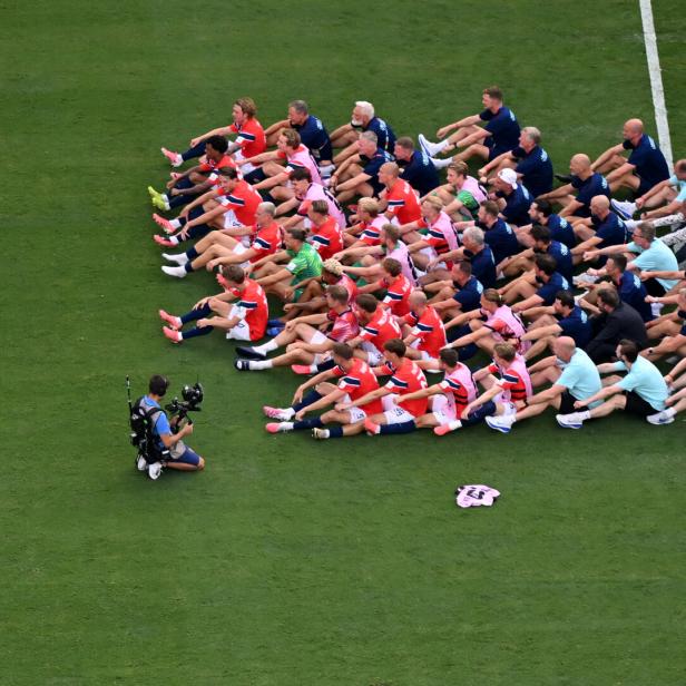 Die Norwegische Nationalmannschaft sitzt auf dem Fußballfeld und macht Ruderbewegungen zum Trommeltakt von E. Haaland