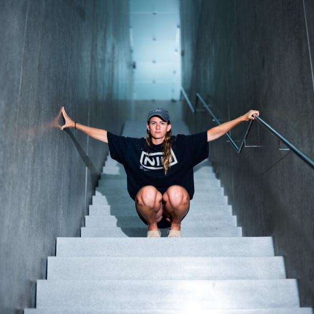 Die Künstlerin Florentina Holzinger mit ausgebreiteten Armen, in der Hocke, auf einer steilen Treppe im Kunsthaus Bregenz, fotografiert von Wolfgang Paterno