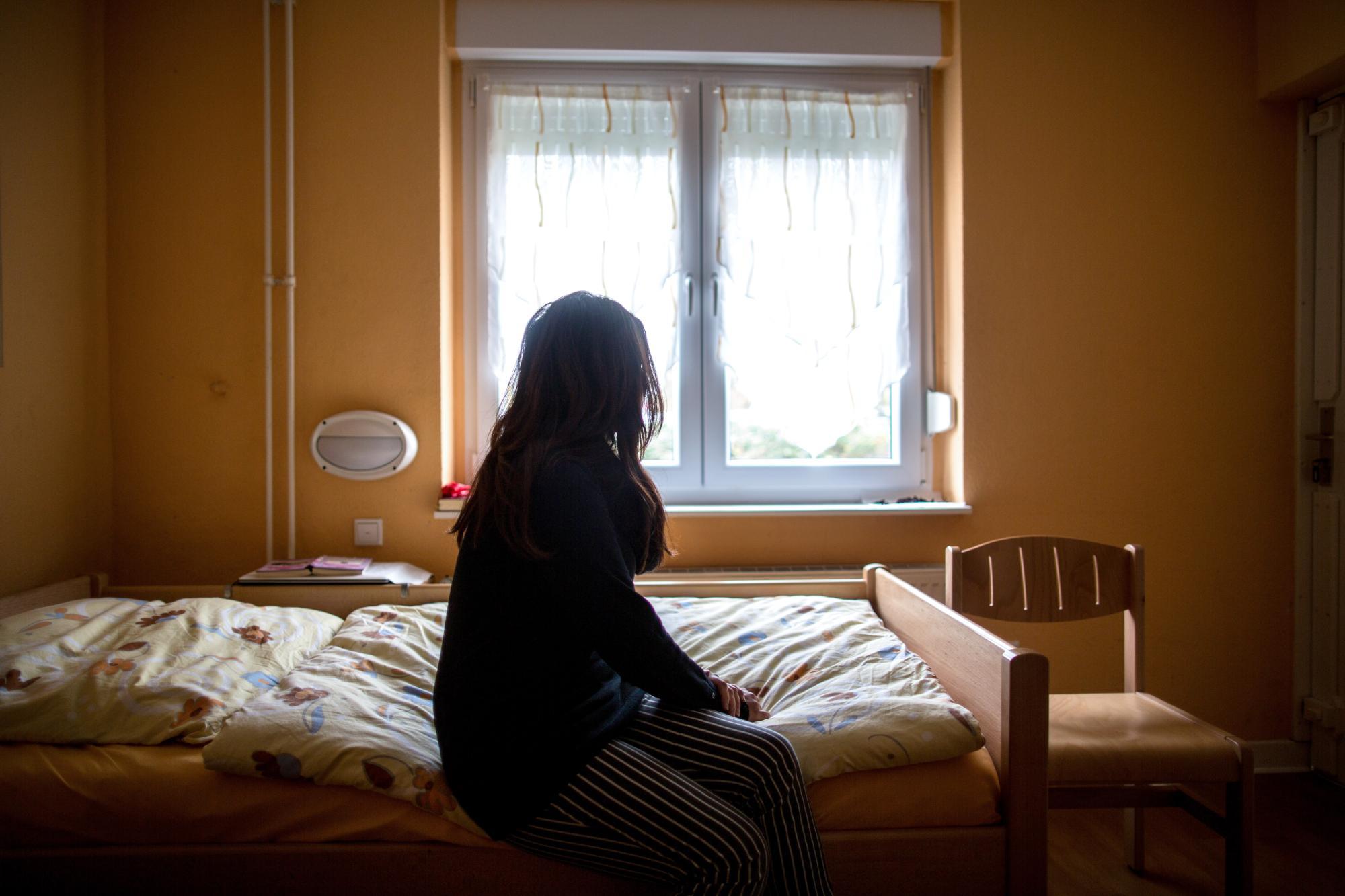 Eine Frau sitzt in einem Frauenhaus auf einem Bett. Frauenhäuser bieten Schutz, wenn der Partner zur Gefahr wird. Dieses Foto stammt von einer Agentur.